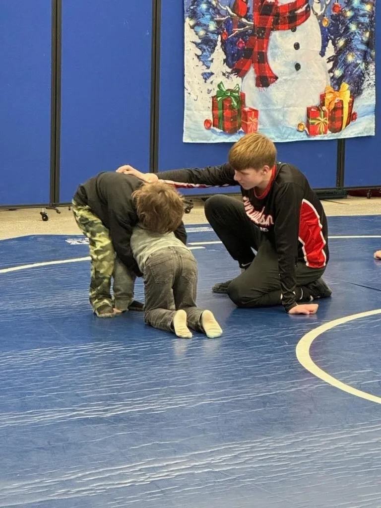 An older student mentoring younger students during wrestling practice