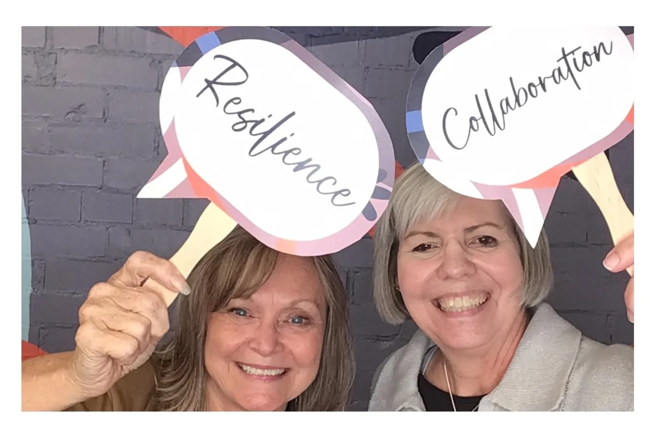 Two smiling CCA staff members holding Resilience and Collaboration signs